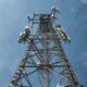 A low-angle shot of a tall metal communications tower with multiple antennas against a clear blue sky.