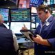 Suasana lantai perdagangan bursa saham Wall Street di New York dengan latar belakang layar indeks pasar yang bergerak variatif.