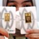Kepingan emas batangan Antam dengan logo perusahaan dan sertifikasi berat di atas latar belakang putih.