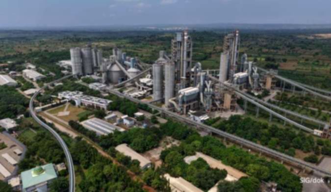 Pekerja memantau operasional mesin di pabrik semen dengan tumpukan material batubara di area industri