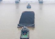 Tumpukan batu bara di area pertambangan dengan latar belakang alat berat dan truk pengangkut